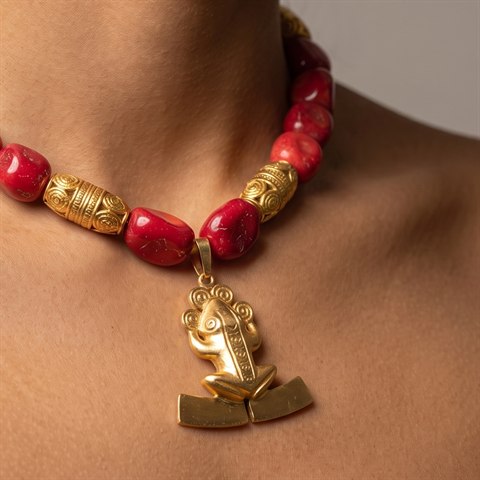 Red coral necklace with a gold frog pendant, worn — symbol of Panamá's Gran Coclé