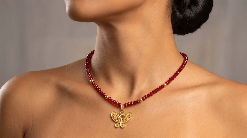Model wearing red crystal beads with a Tairona butterfly nariguera in gold filigree