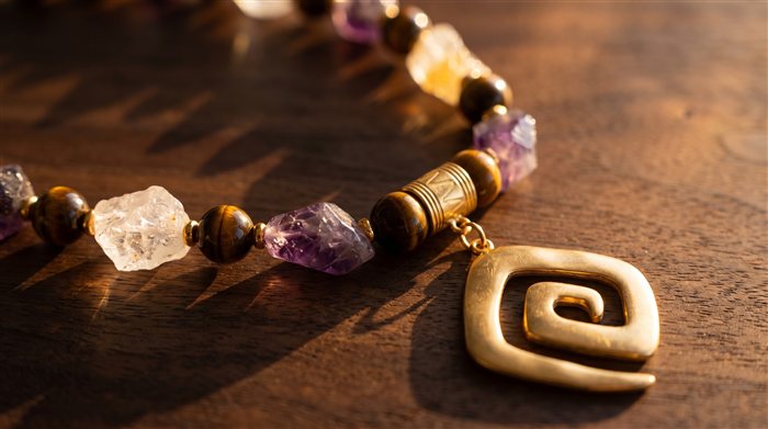 Amethyst, quartz and tiger's eye necklace with a gold Calima-spiral pendant, on wood at sunset