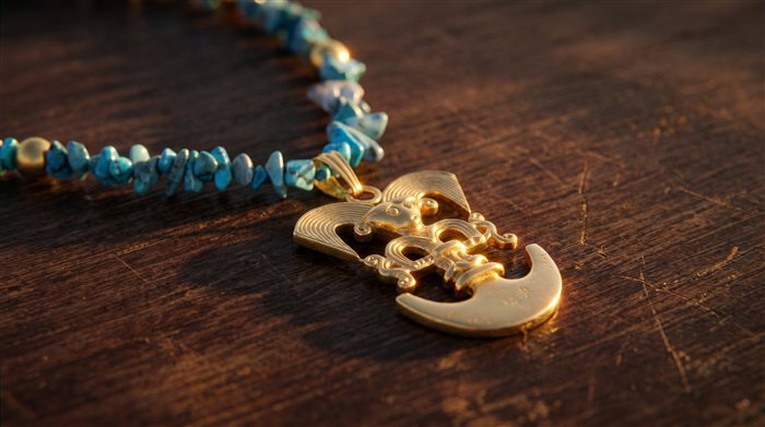 Turquoise chip necklace with a gold bird-beaked man pendant, on wood at sunset