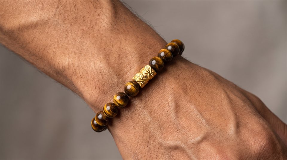 Man wearing a tiger's eye bead bracelet with an engraved gold greca bead