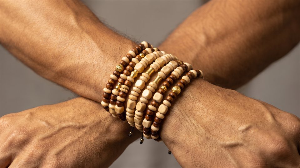 Man wearing stacked wood bead bracelets in cream and brown on crossed wrists