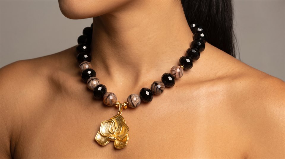 Model wearing black and grey agate beads with an engraved gold flower pendant
