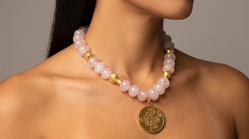 Model wearing rose quartz beads with a gold medallion engraved with the saurian deity